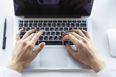 Businessman typing on laptop keyboard in sunny office, business and technology concept. Close up