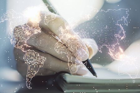 Abstract creative world map and woman hand writing in notebook on background, international trading concept. Multiexposureの写真素材