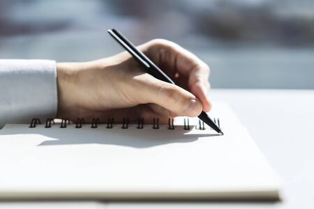 Man writes with a pen in notepad in a sunny office, business and education concept. Close upの写真素材