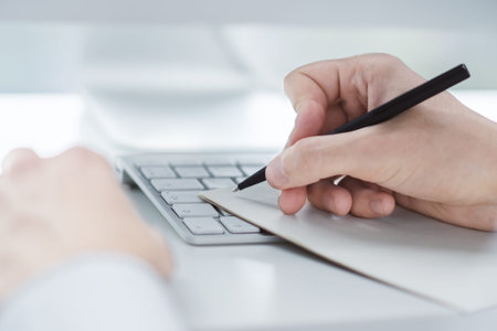 Man writes with a pen in notepad on computer keyboard in a sunny office, business and education...