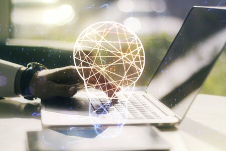 Creative light bulb hologram with hands typing on computer keyboard on background, idea concept. Multiexposureの写真素材