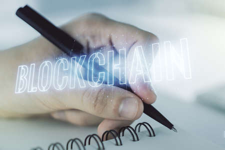 Double exposure of blockchain technology hologram and man hand writing in notebook on background. Research and development decentralization software conceptの写真素材