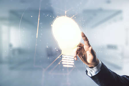 Male hand clicks on abstract virtual light bulb illustration on blurred office background, future technology concept. Multiexposureの写真素材