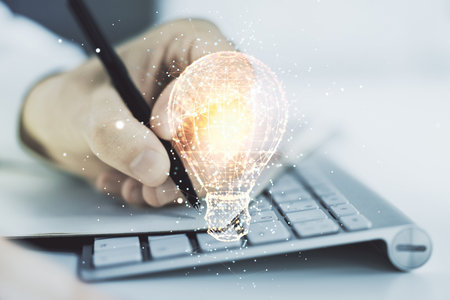 Creative light bulb hologram with hand writing in notepad on background with laptop, idea concept. Multiexposureの写真素材