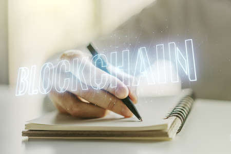 Creative abstract blockchain technology hologram and man hand writing in diary on background, cryptography and decentralization concept. Multi exposureの写真素材