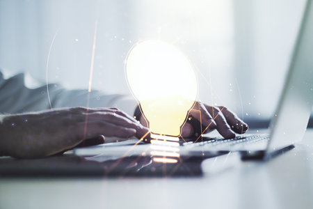 Creative light bulb hologram with hands typing on computer keyboard on background, idea concept. Multiexposureの写真素材