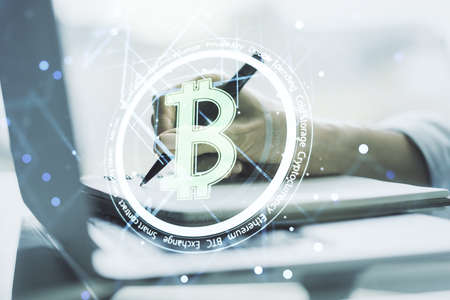 Double exposure of creative Bitcoin symbol hologram with hand writing in notepad on background with laptop. Mining and blockchain conceptの写真素材
