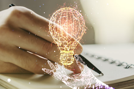 Creative light bulb hologram with hand writing in notepad on background, idea concept. Multiexposureの写真素材