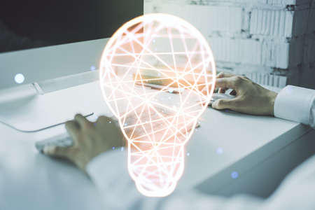 Creative light bulb hologram with hands typing on computer keyboard on background, idea concept. Multiexposureの写真素材