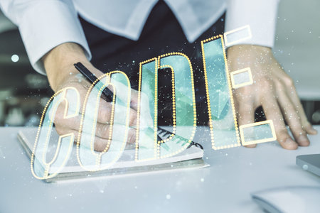 Creative Code word hologram and hand writing in notepad on background with laptop, artificial...