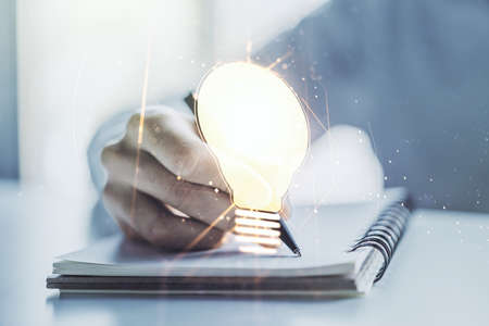Creative light bulb hologram with hand writing in notepad on background, idea concept. Multiexposureの写真素材