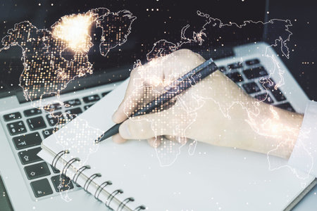 Double exposure of abstract digital world map and hand writing in notepad on background with laptop,...
