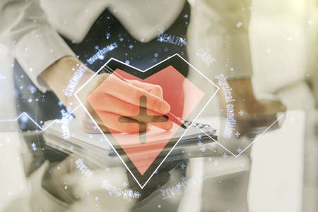 Double exposure of creative abstract heart rate hologram and man hand writing in notebook on background. Healthcare technolody conceptの写真素材