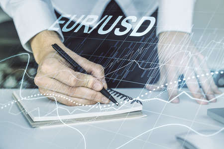 Double exposure of creative EURO USD forex chart hologram and hand writing in notebook on background with laptop. Banking and investing conceptの写真素材