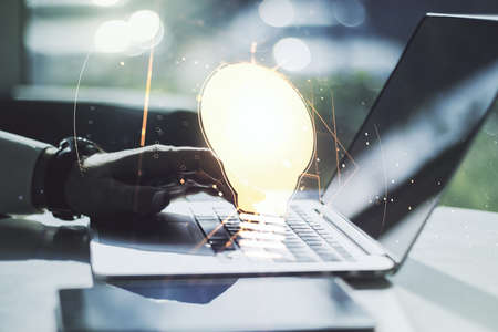 Double exposure of creative light bulb hologram with hands typing on laptop on background, research and development conceptの写真素材