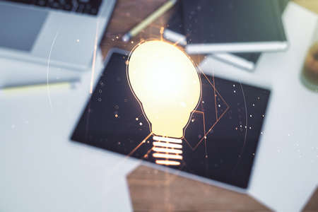Creative light bulb hologram and modern digital tablet on background, idea concept. Multiexposureの写真素材