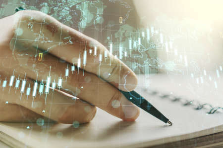 Multi exposure of abstract financial diagram with world map and with man hand writing in notepad on background, banking and accounting conceptの写真素材