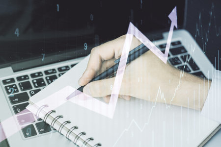 Double exposure of abstract creative financial chart with upward arrow and hand writing in notebook on background with laptop, research and strategy conceptの写真素材