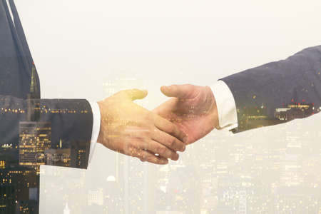 Multi exposure of handshake of two businessmen on city skyscrapers background, collaboration and teamwork conceptの写真素材
