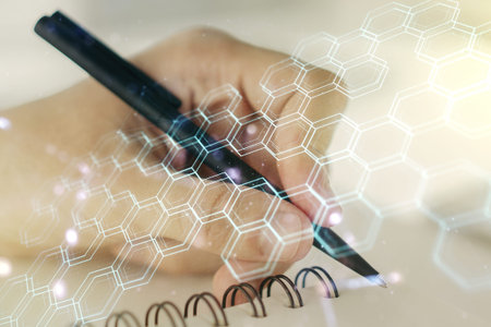 Double exposure of technology hologram with hexagon and man hand writing in notebook on background....