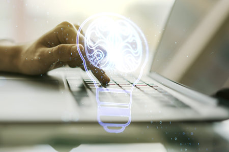 Double exposure of creative light bulb hologram with human brain and with hands typing on laptop on...