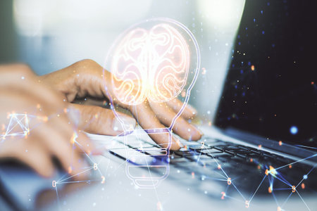Creative light bulb with human brain hologram and with hands typing on computer keyboard on...