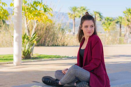 Attractive girl with red jacket sitting on a bench in the park.の写真素材