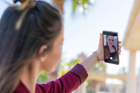 Defocused young woman seen from behind with a mobile phone in her hand and taking a selfie,の写真素材