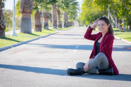 Young woman with glasses and cheerful sitting in the middle of a road with palm treesの写真素材
