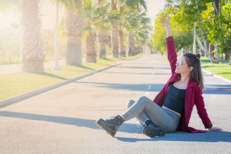 Young woman with glasses and cheerful sitting in the middle of a road with palm treesの写真素材