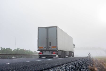 Truck with refrigerated semi-trailer driving on the highway on a thick foggy dayの写真素材