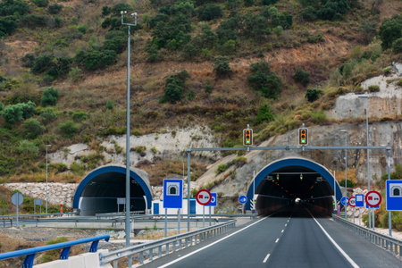 Entrance to a tunnel on the highway with various traffic signals and traffic lights.