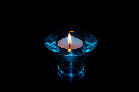 Blue glass candle holder with dark background, with lit candle.の写真素材