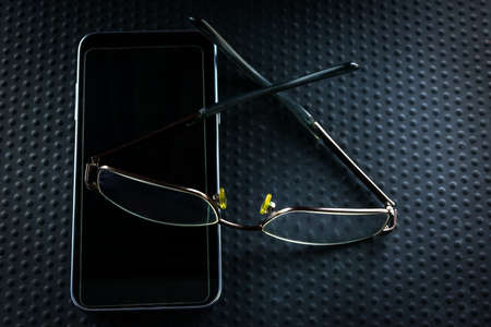 Reading glasses on a mobile phone on a black backgroundの写真素材