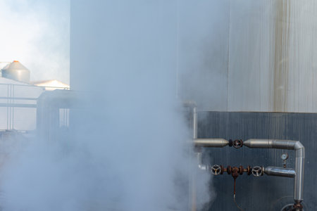 Pipes for liquids at high temperature next to a tank and giving off steam.の写真素材