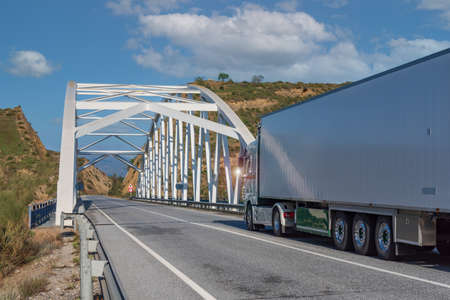 Truck with refrigerated semi-trailer on a mountain road and going over an iron bridge.
