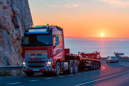 Truck dedicated to special transport on a mountain road with the sea and the sun in the background...