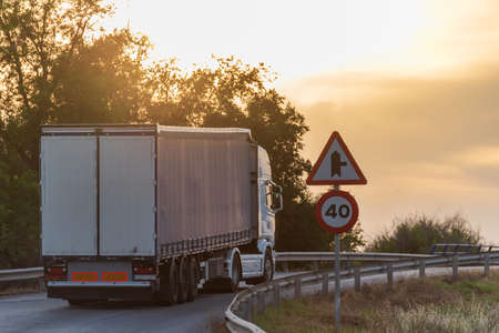 Truck with semi-trailer for general cargo reaching a limited speed crossing at sunset.の写真素材