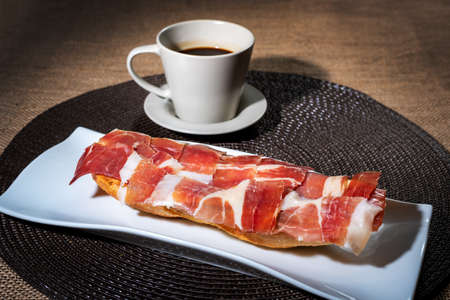 Breakfast consisting of a coffee and a Serrano ham toast with olive oil and tomato.の写真素材