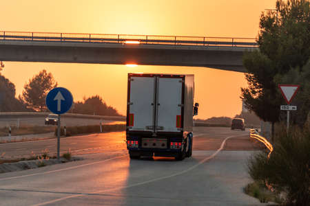 Truck with refrigerated semi-trailer driving on the highway with the sun in front of it at sunset.の写真素材