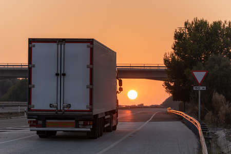 Container truck driving on the highway with the sun in front of it at sunset.の写真素材