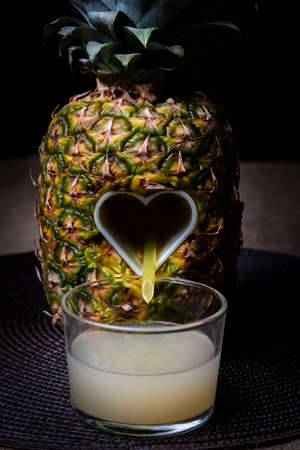 Pineapple with an open heart in the center from which the juice flows into a glass.の写真素材