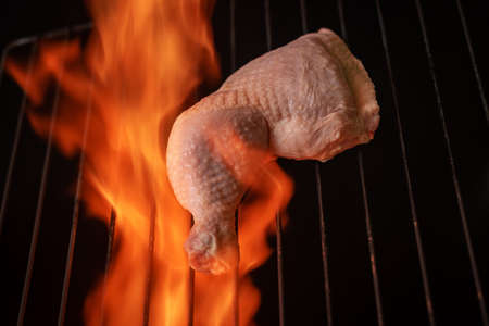 Raw chicken thigh on a grill with fire around it. Foreground.の写真素材
