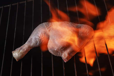 Raw chicken thigh on a grill with fire around it. Foreground.の写真素材
