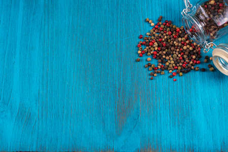Blue wooden background with a lying pot with multi-colored peppercorns. Copy space.の写真素材