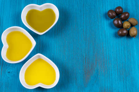 Blue wooden background with several sauce boats with different types of olive oil, next to several olives.の写真素材