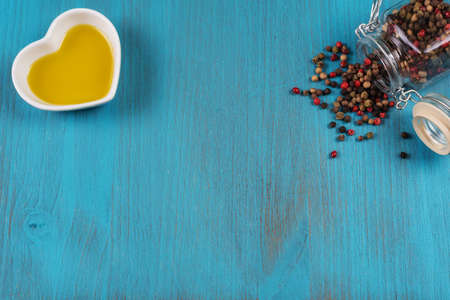 Blue wooden background with a lying pot with peppercorns of various colors and a small bowl with olive oil. Copy space.の写真素材