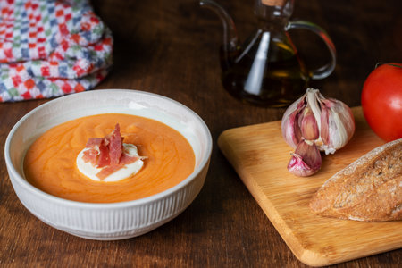 Round plate with salmorejo, ham and egg, along with some tomatoes, bread and garlic, ingredients used for its preparation.の写真素材