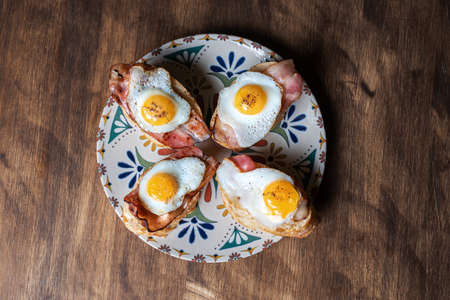 Slice of bread with bacon and grilled quail egg, on a wooden table.