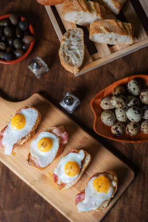 Slice of bread with bacon and grilled quail egg, on a wooden table.の写真素材